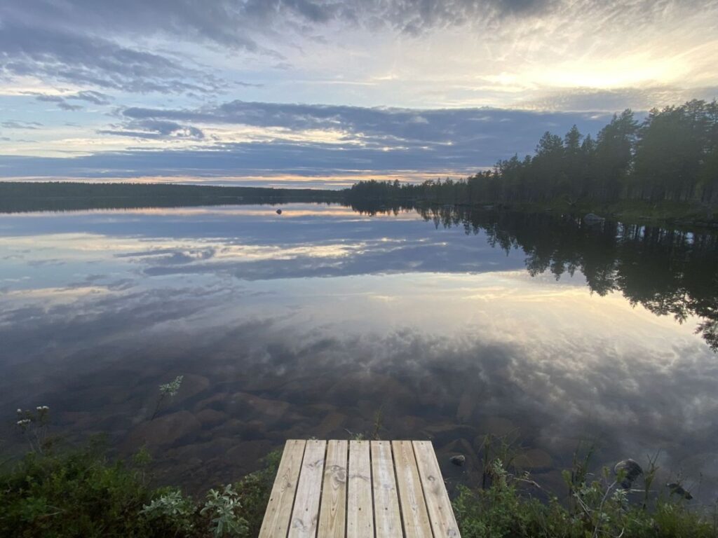 golden sky and mirror lake with dock in arjeplog